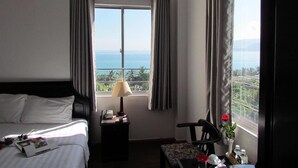A hotel room with a bed, a nightstand with a lamp, a small table with a chair, and a window with a view of the sea. - Dream Hotel Nha Trang (Nha Trang)