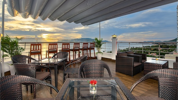 A rooftop terrace with wicker furniture, a glass table with a vase, and a view of the sunset over the sea. - Dream Hotel Nha Trang (Nha Trang)