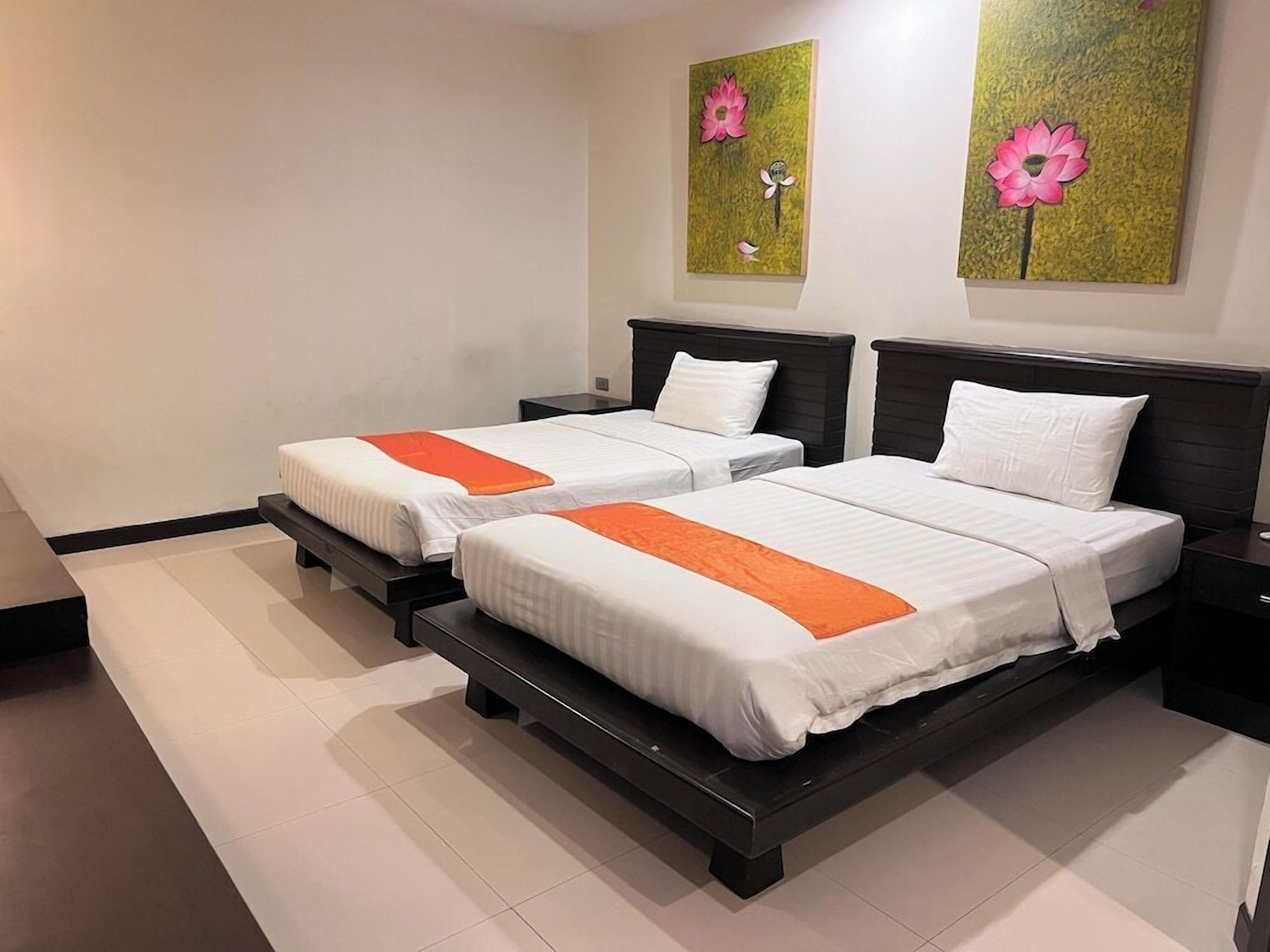 Ein Hotelzimmer mit zwei Betten, weißer Bettwäsche, orangefarbenen Akzenten und floralen Bildern an den Wänden.