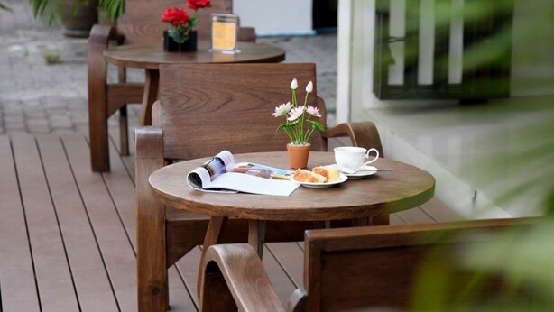 Una mesa de madera al aire libre con una revista, una taza y un plato de comida.
