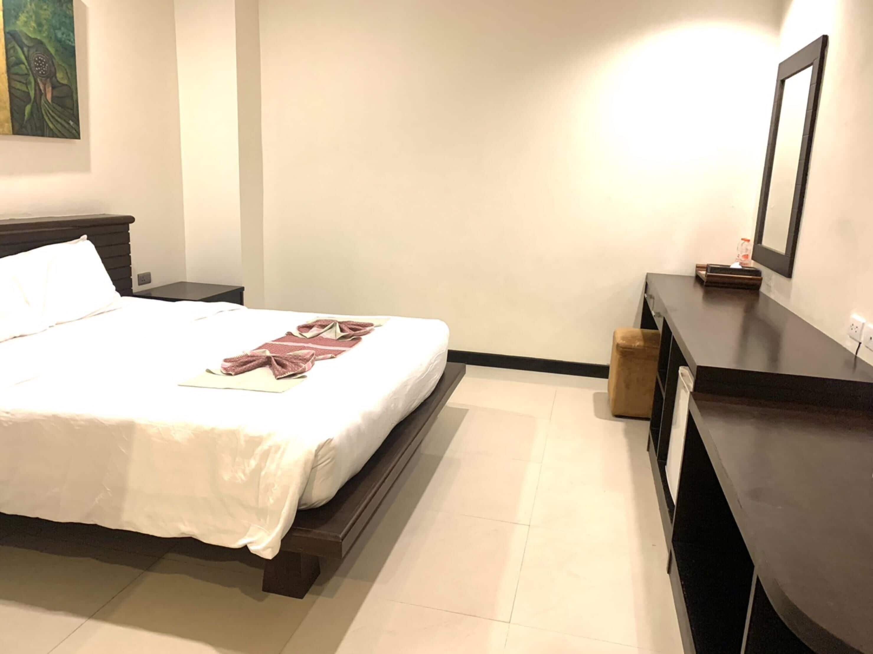 A hotel room with a bed, a nightstand, a dresser, and a painting on the wall.