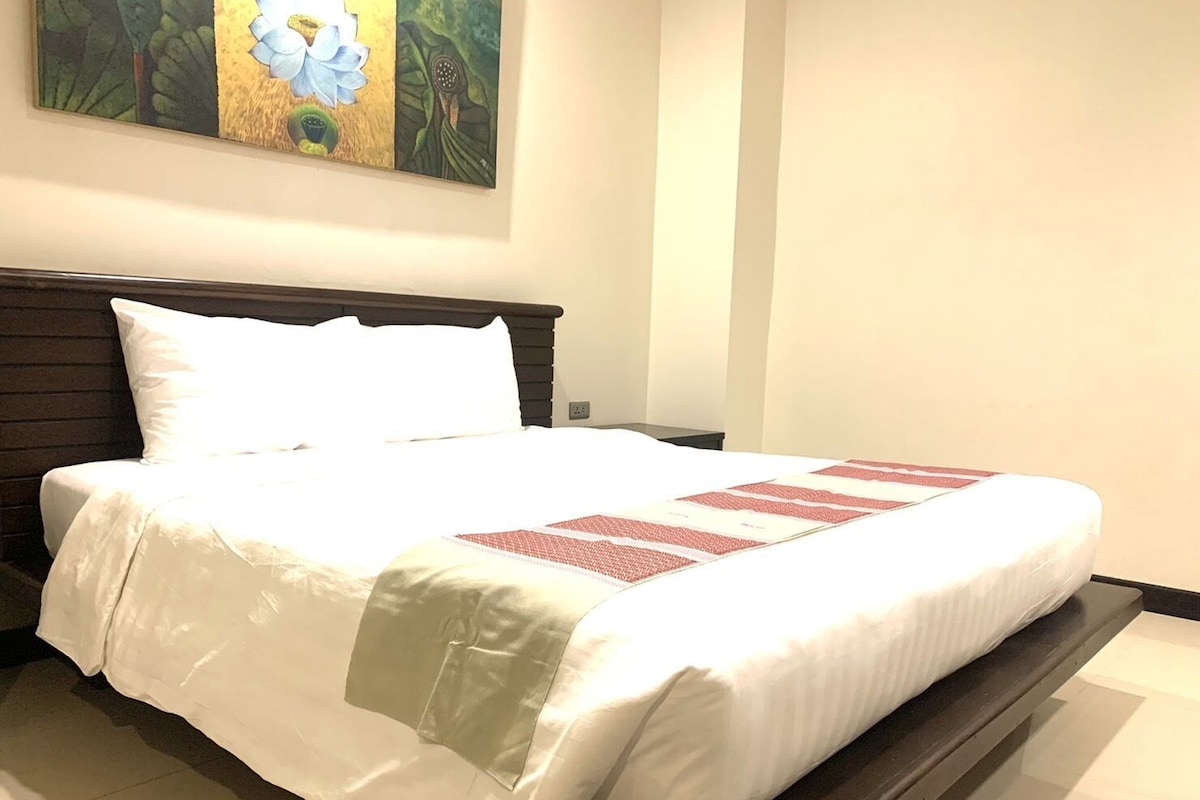 A neatly made bed with white linens and a red and white patterned throw.