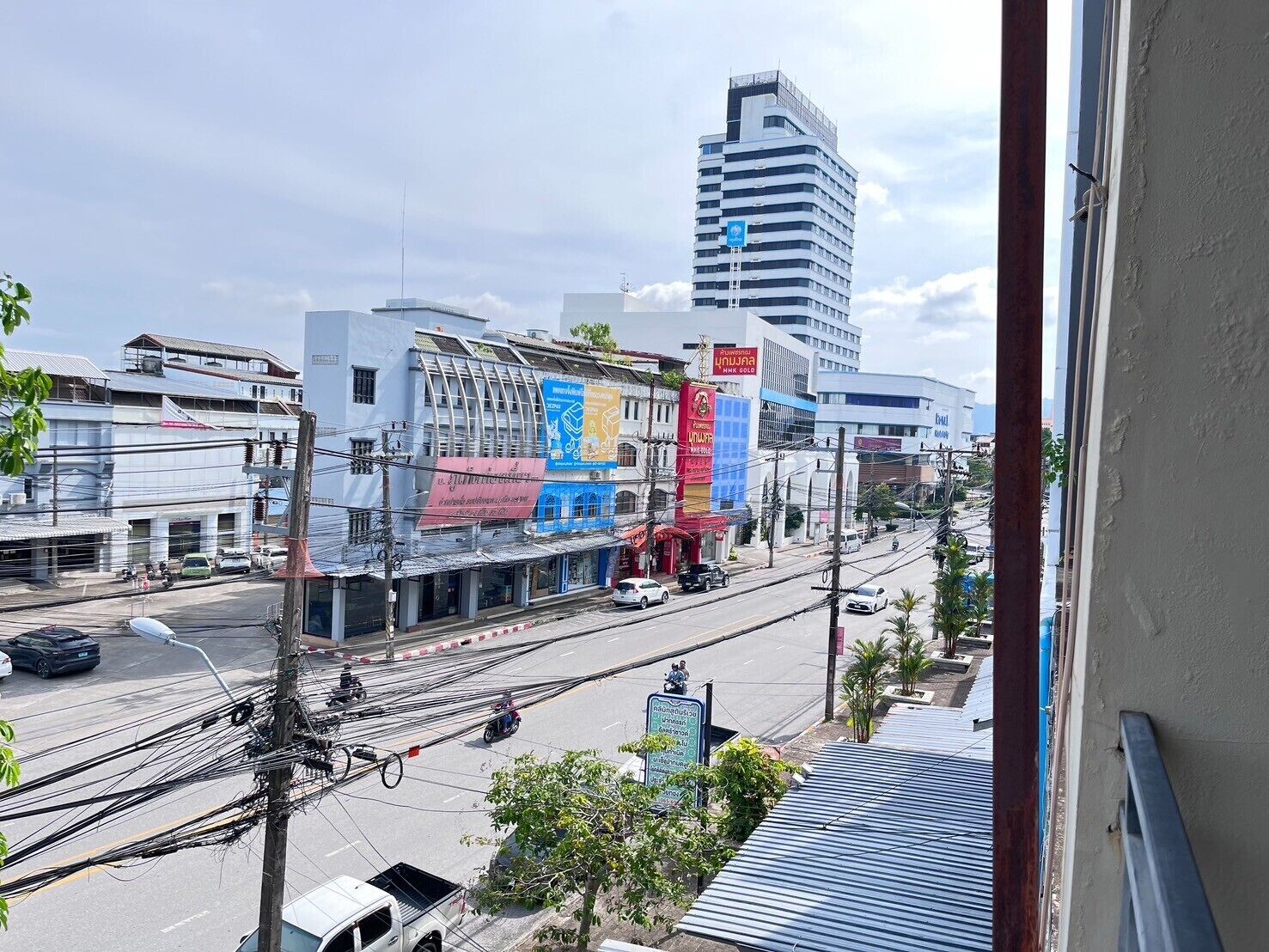 A street view with a building featuring a large signboard, a tall building in the background, and a clear sky.