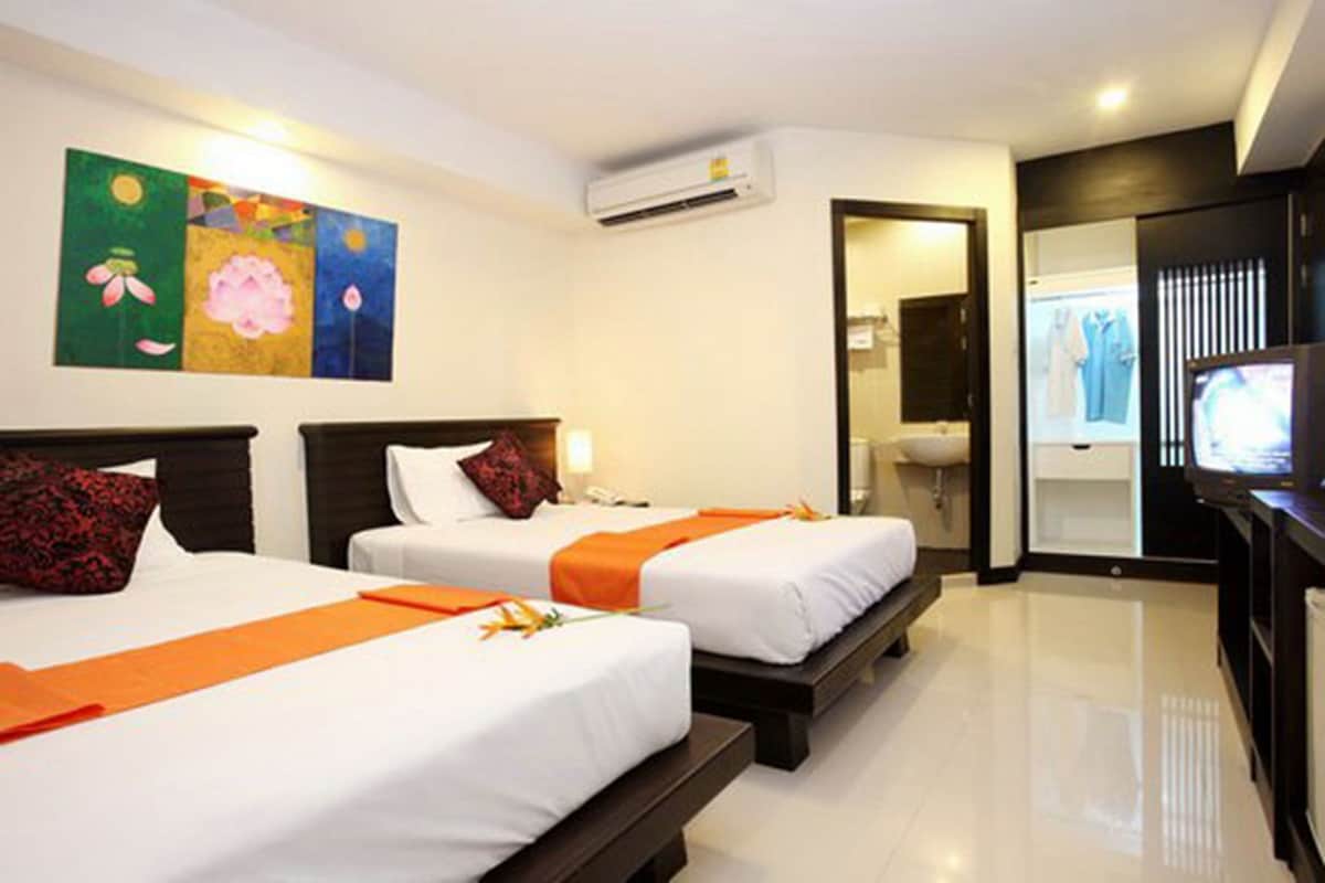 A hotel room with two beds, an air conditioning unit, a television, and artwork on the wall.