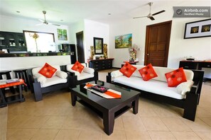 A modern living room with a sofa set, coffee table, and a kitchen area in the background. - Zen Villa Bali (Denpasar)