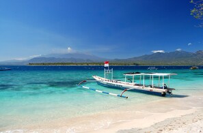 A boat named 'Monco Dive' docked at a beach with clear turquoise water and a mountain in the background. - Zen Villa Bali (Denpasar)