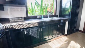 Una cocina moderna con armarios oscuros, encimera negra y ventana con vistas a plantas verdes.