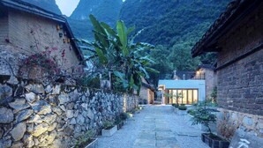 A traditional courtyard with stone walls, a pathway, and a building with large windows. - XY YunHouse (Guilin)
