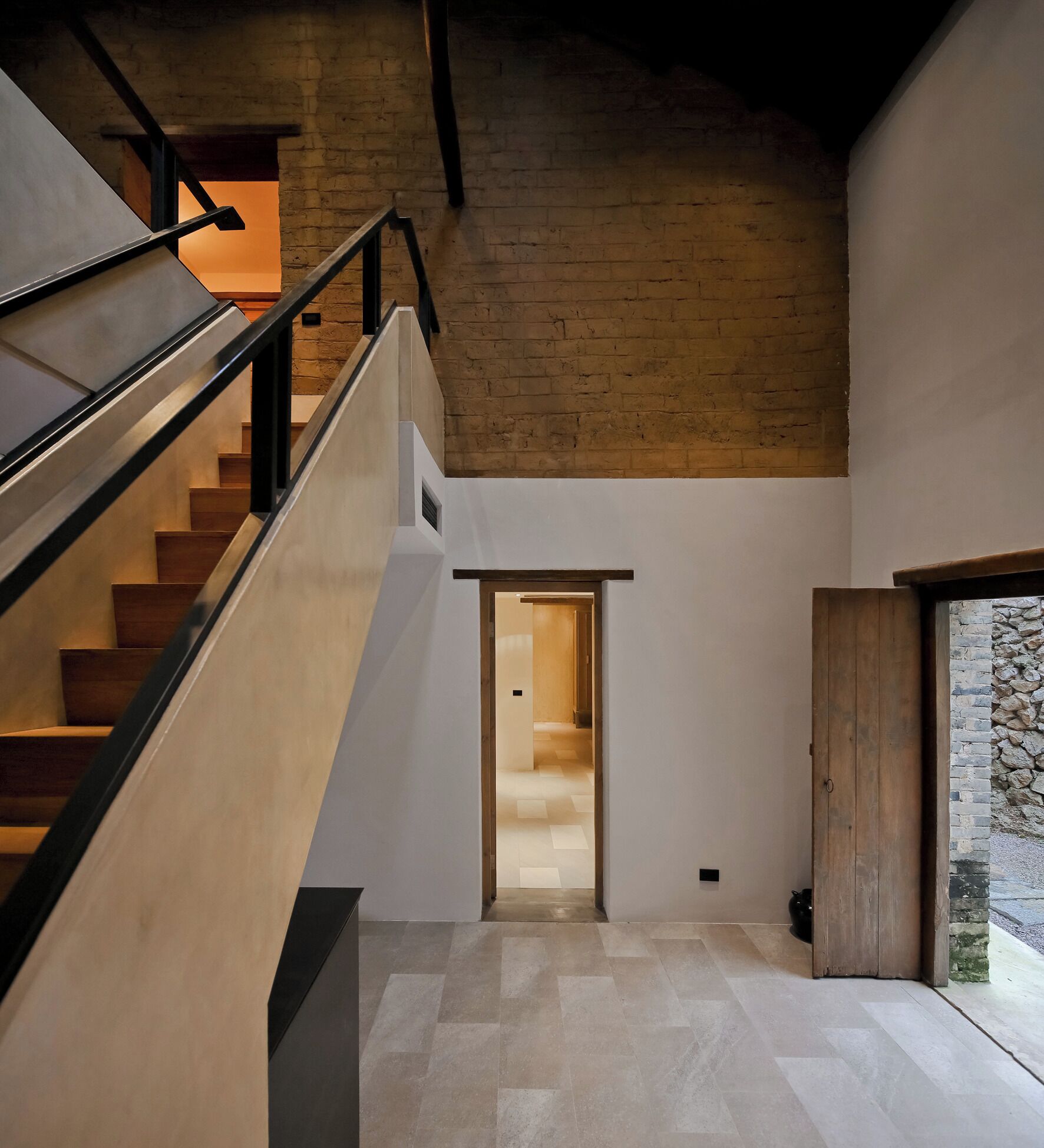 Un intérieur moderne avec un escalier menant à un deuxième étage, une porte en bois et une vue sur l’extérieur.