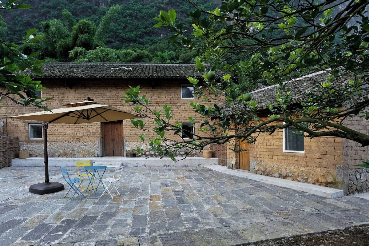 A courtyard with a brick building, a table with chairs, and a large umbrella.