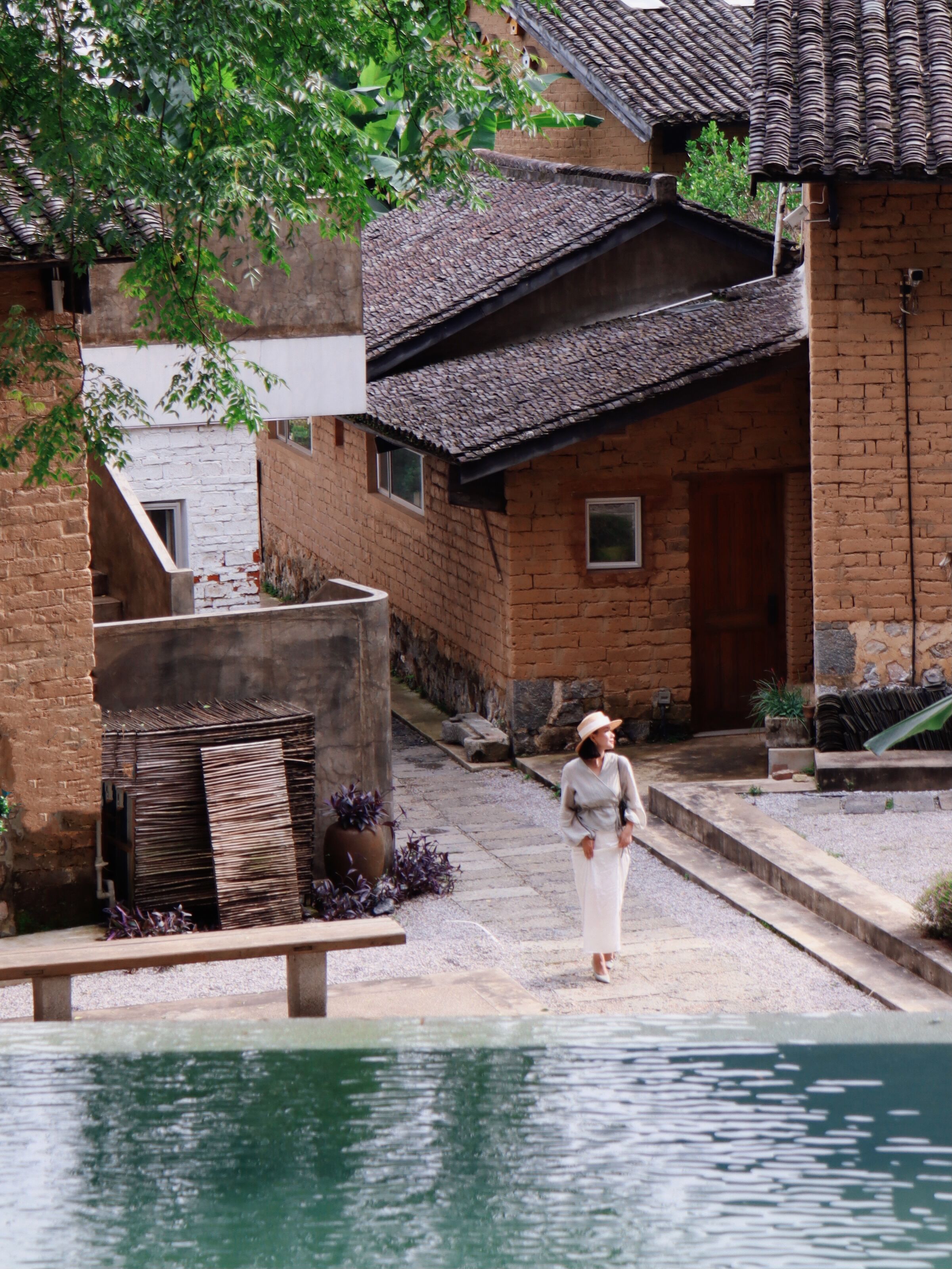 A traditional brick building with a tiled roof, a stone staircase, and a pool in the foreground.