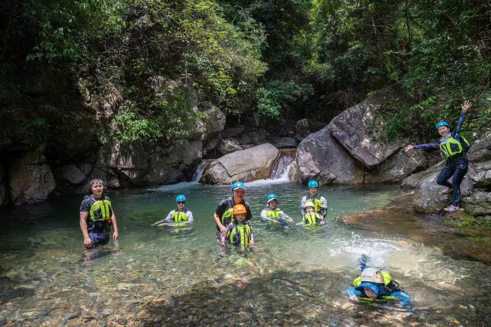 Un gruppo di persone in un ambiente naturale, con acque limpide, circondato da rocce e vegetazione.