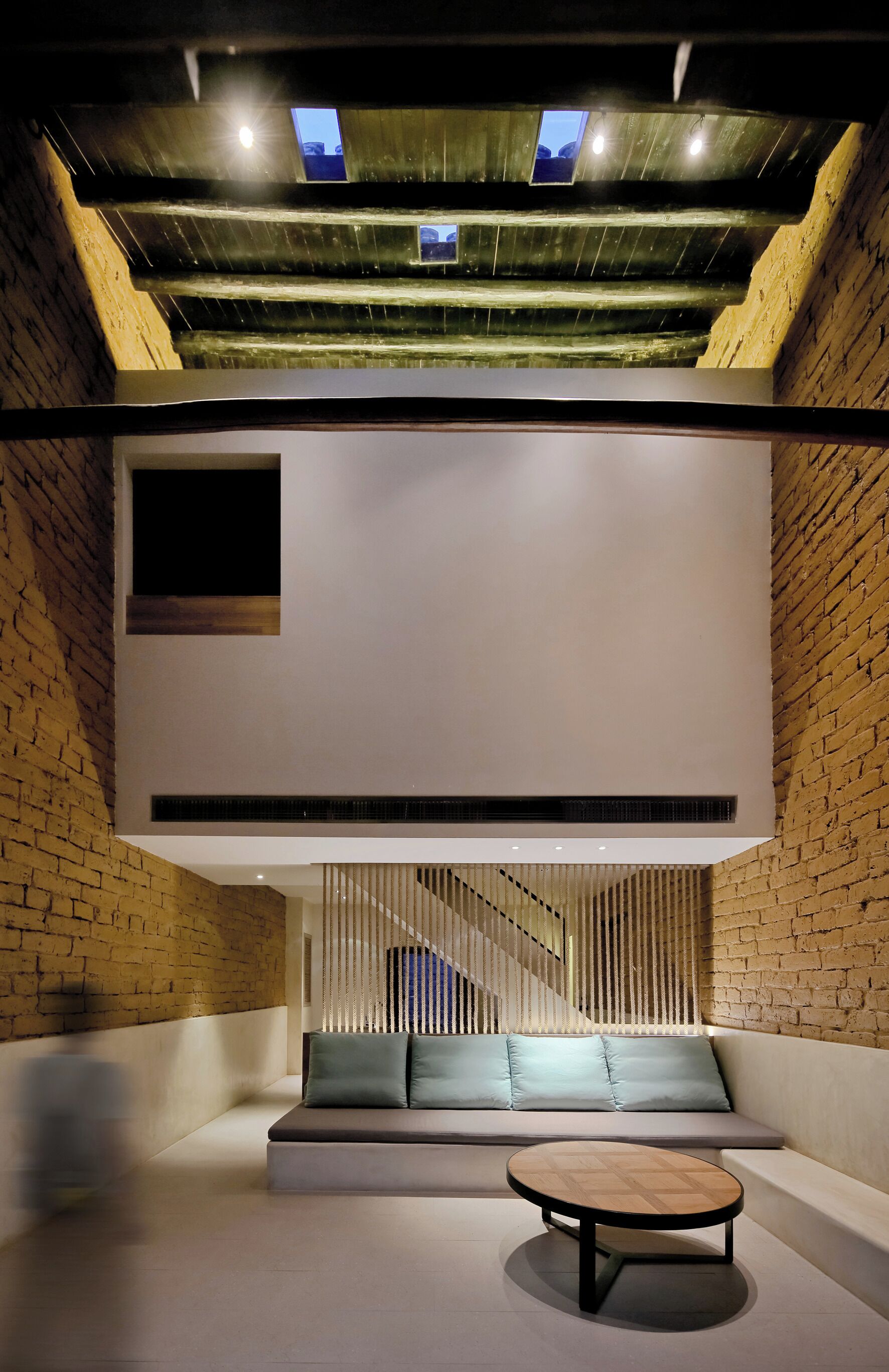 A modern interior with a brick wall, a wooden ceiling, a seating area with cushions, and a round table.