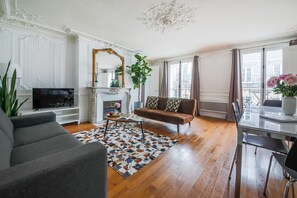 A living room with a sofa, a coffee table, a TV, and a fireplace. - Résidence Bergère - Appartements (Paris)