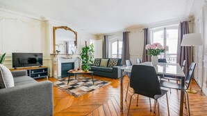 Uma sala de estar com sofá, televisão, mesa de jantar, cadeiras e lareira.