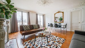 Uma sala de estar com um sofá marrom, uma mesa de centro com um tabuleiro de petiscos, um tapete estampado e um espelho grande com moldura dourada.
