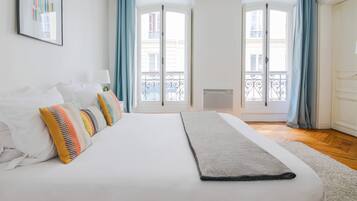 A bedroom with a large bed, a view of the outside balcony, and a door leading to the balcony.