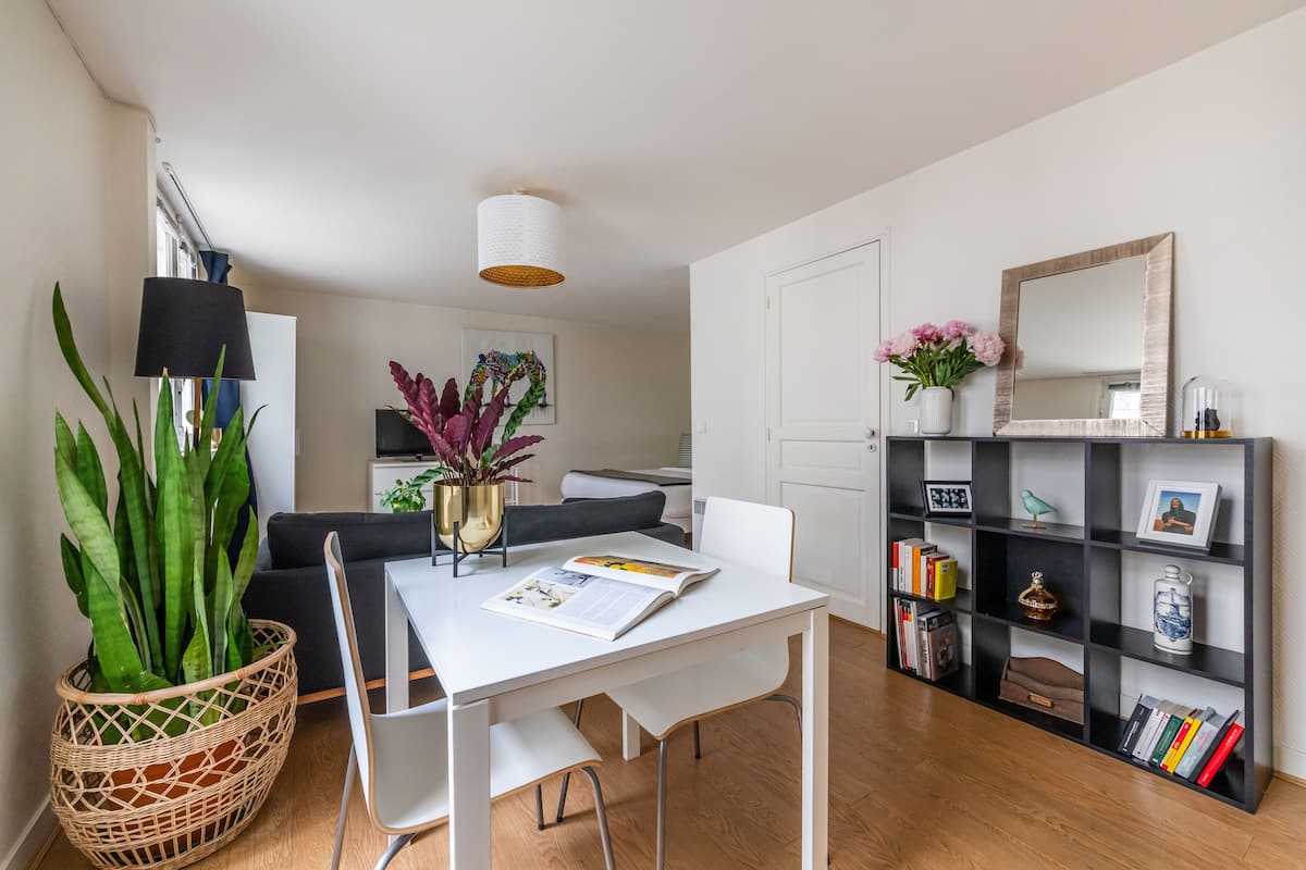 Un salon moderne avec une table blanche, un canapé noir et une bibliothèque remplie de livres et d’objets décoratifs.