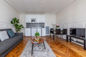 A modern living room with a sofa, coffee table, TV, and dining area. - Résidence Bergère - Appartements (Paris)