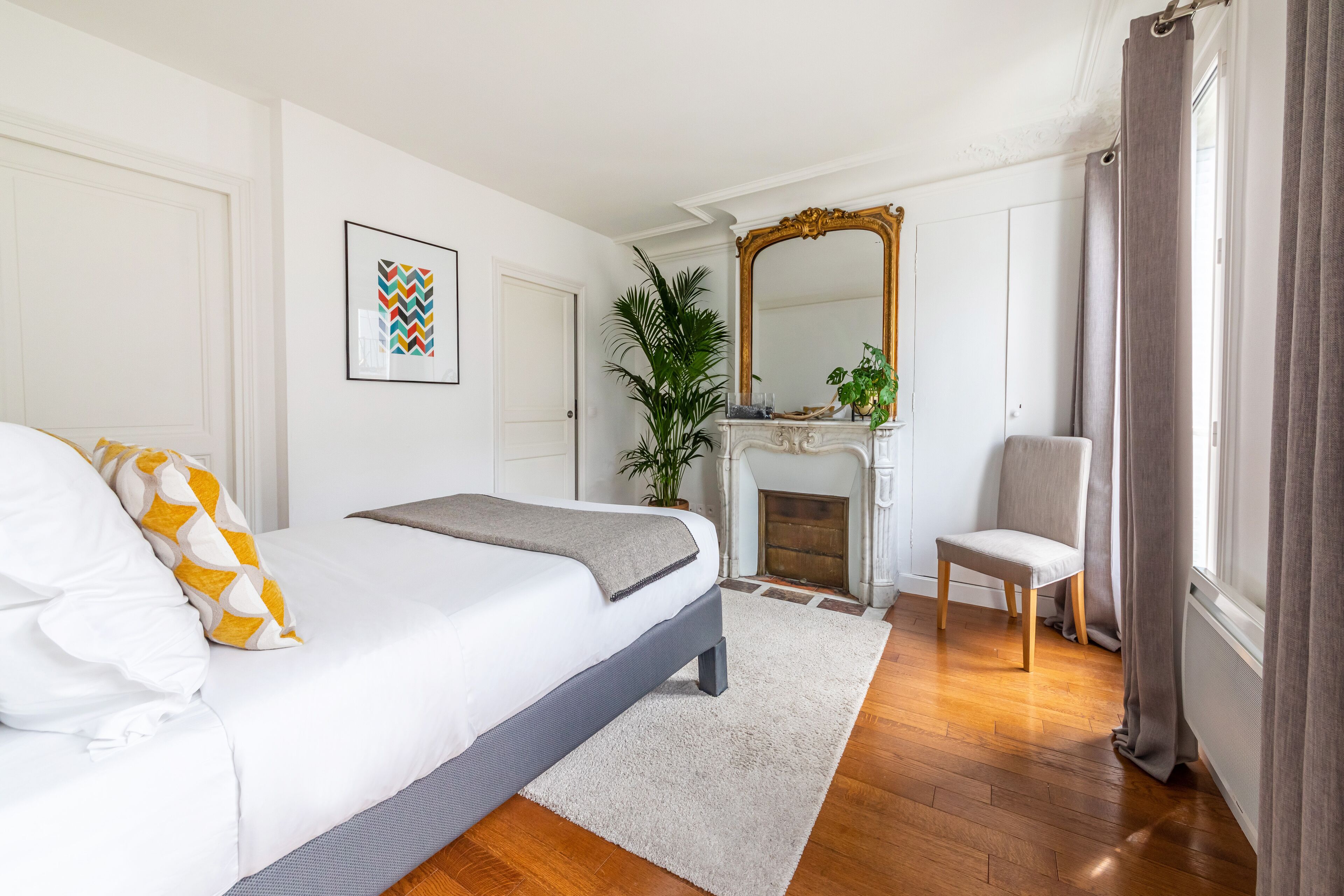 Une chambre à coucher avec un lit, une chaise, une cheminée et un miroir.