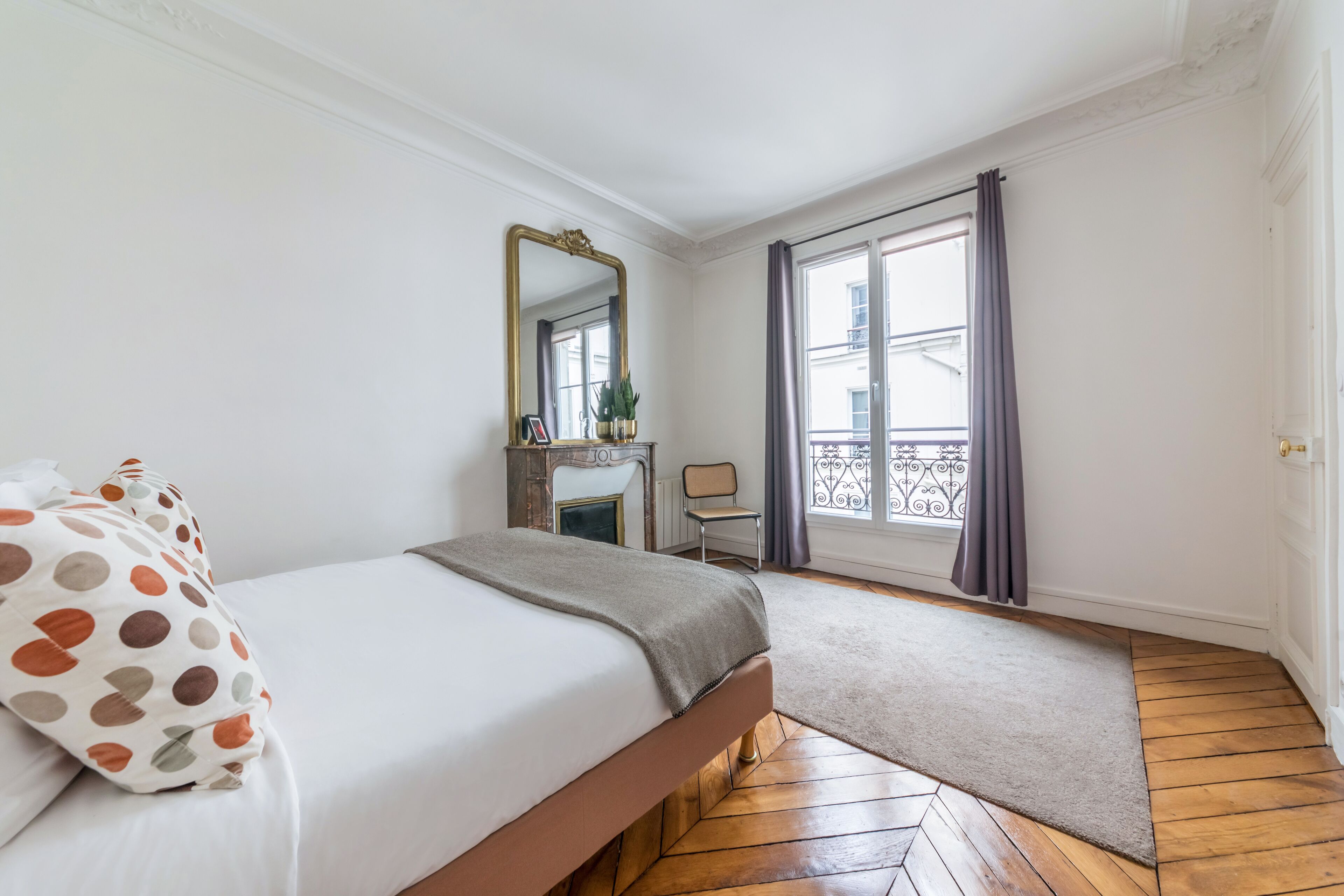 Una camera da letto con un letto, una cassettiera, uno specchio, una finestra con tende e un pavimento in legno.