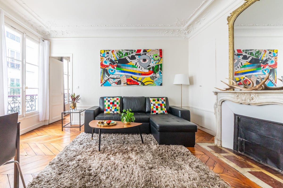 Un salon avec un canapé noir, un tapis moelleux et une cheminée.