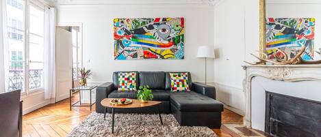 Een woonkamer met een zwarte bank, een pluizig vloerkleed en een open haard.