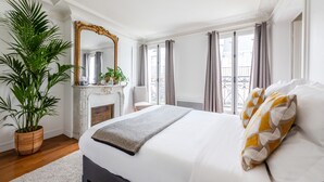 Quarto com uma cama grande, uma planta em vaso, lareira e vista para o exterior.