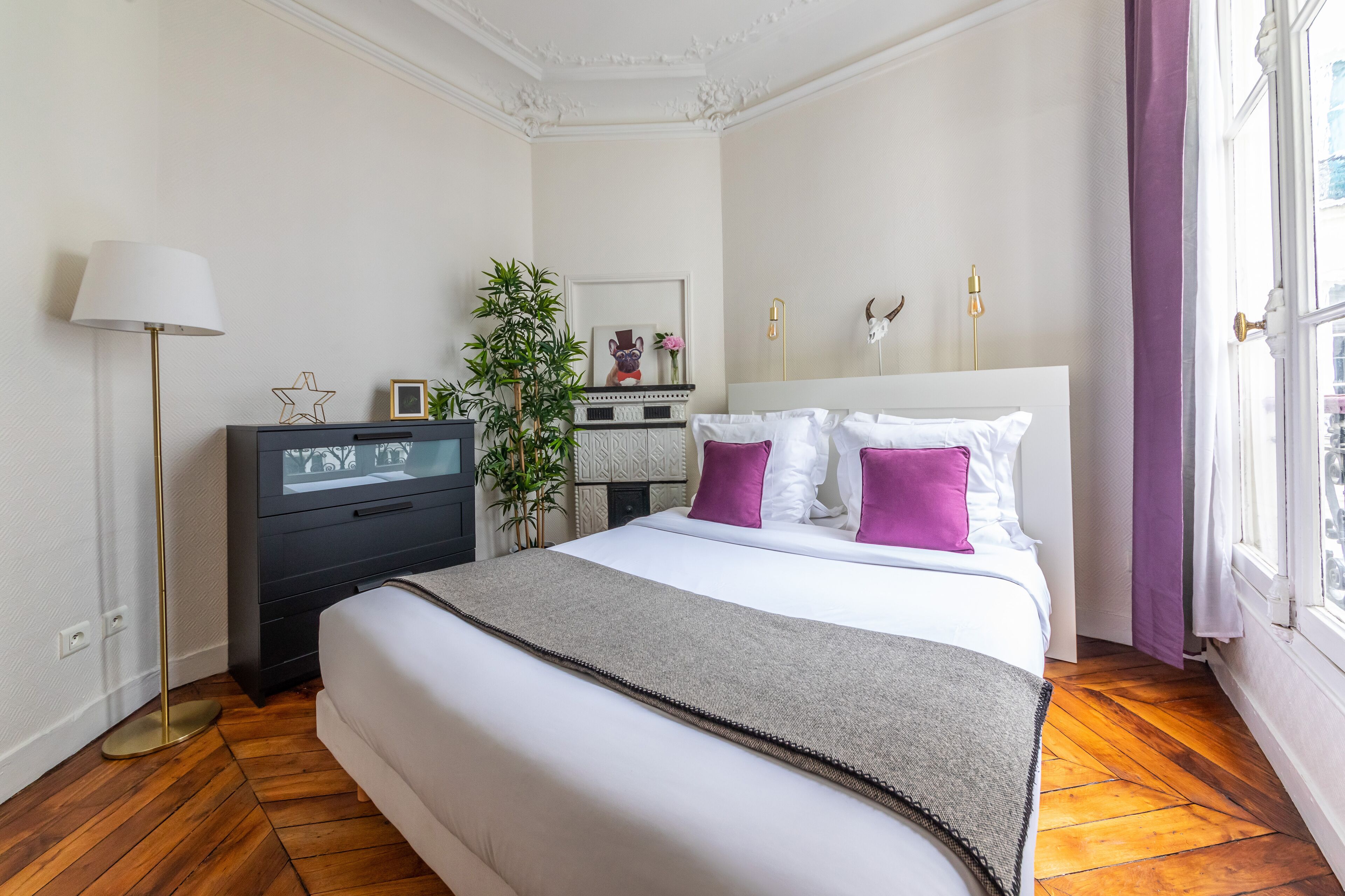 A neatly arranged bedroom with a bed, bedside table, lamp, and a potted plant.
