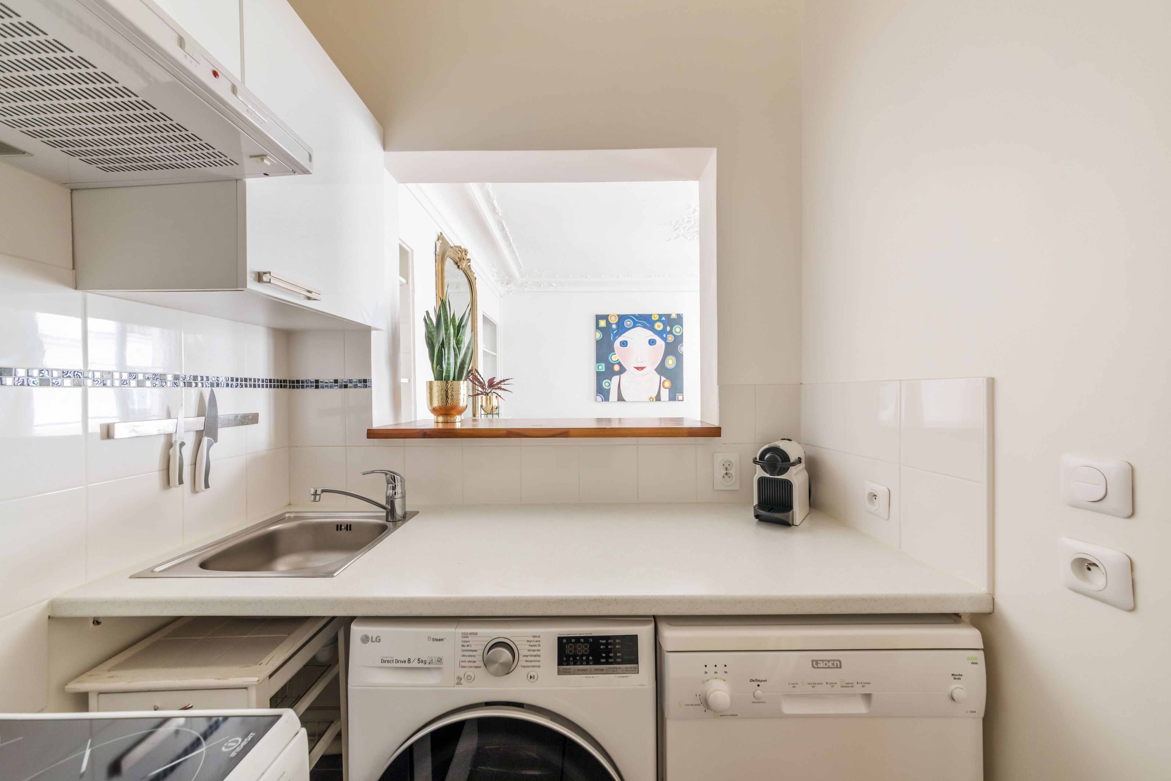 A compact kitchen with a built-in washing machine, a sink, and a window with a view of the city.