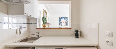 A compact kitchen with a built-in washing machine, a sink, and a window with a view of the city.