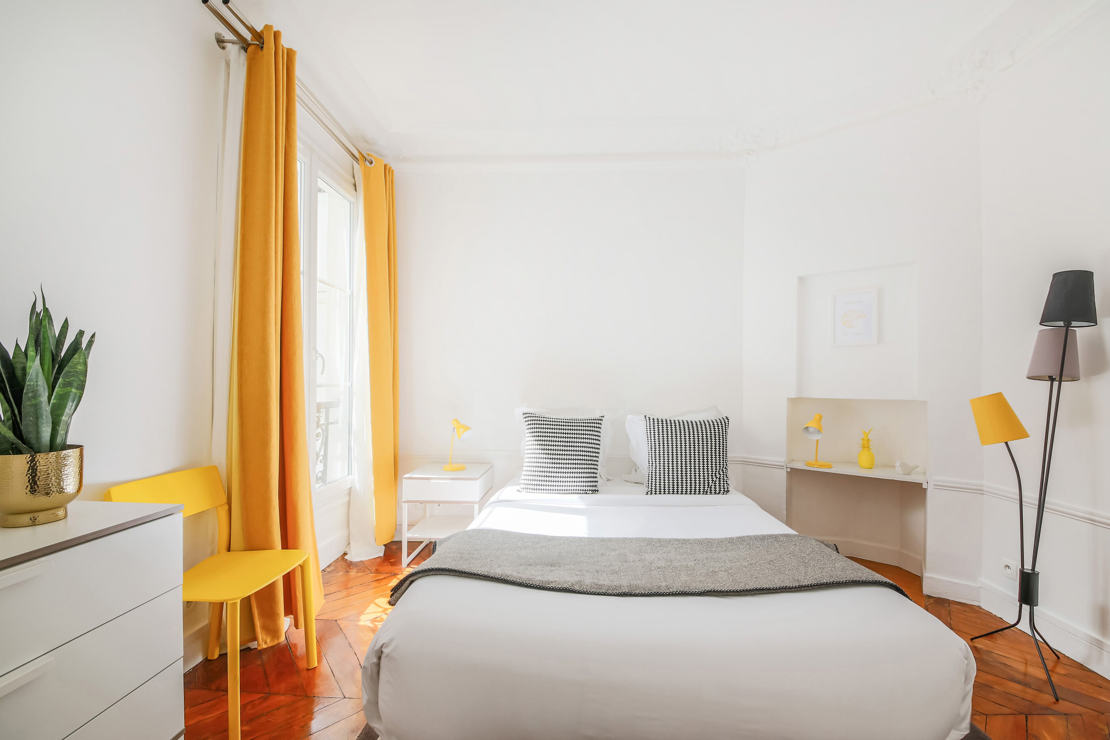 A modern bedroom with a bed, bedside tables, a desk, a chair, a potted plant, and a floor lamp.