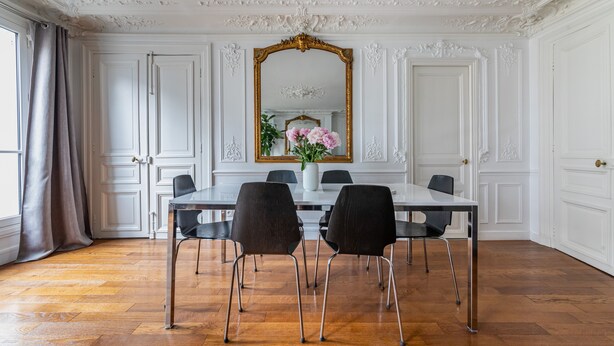 Uma sala de jantar com teto branco ornamentado, um espelho grande e uma mesa com quatro cadeiras.