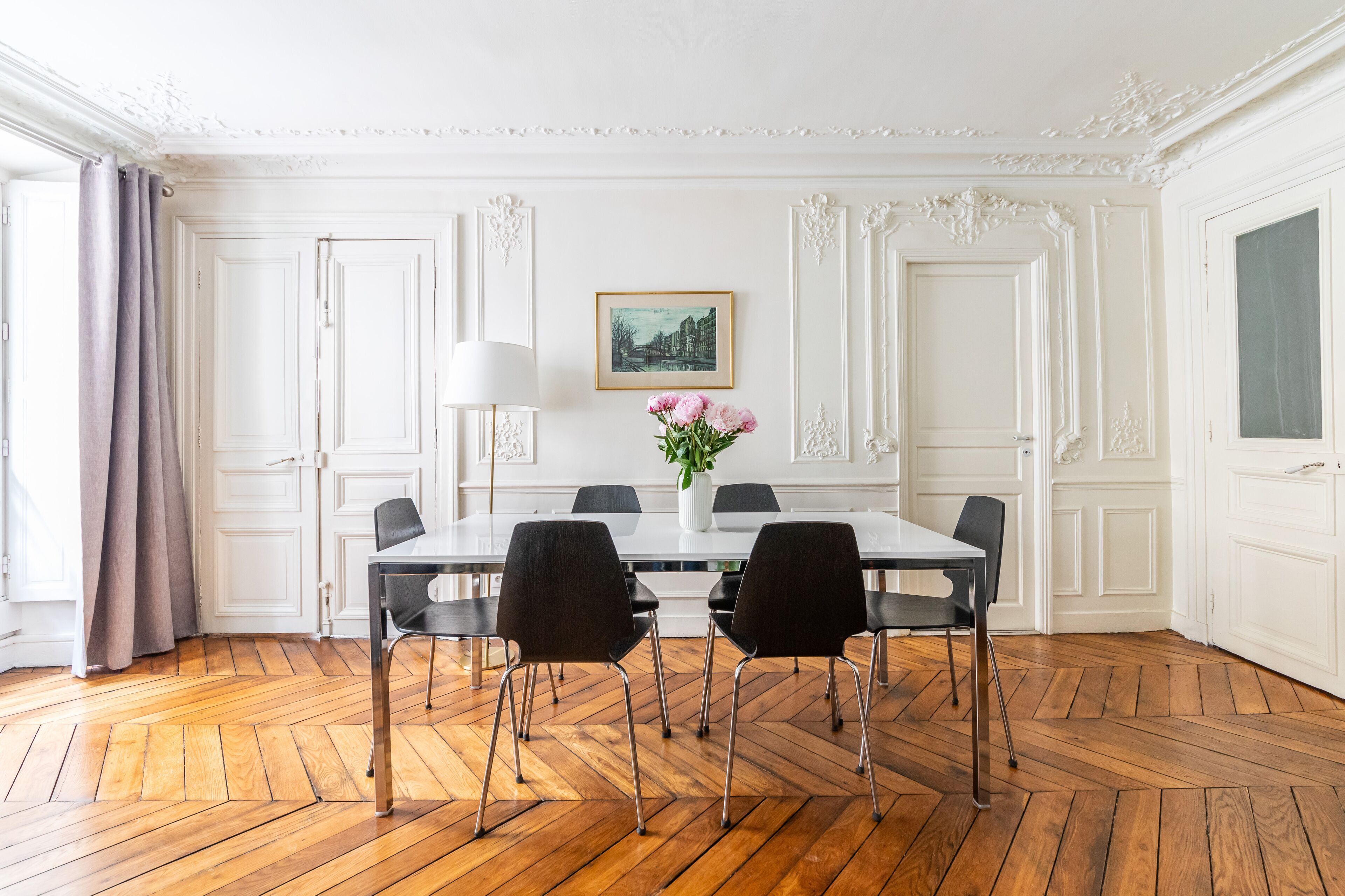 A dining room with a white table, black chairs, and a vase of flowers.