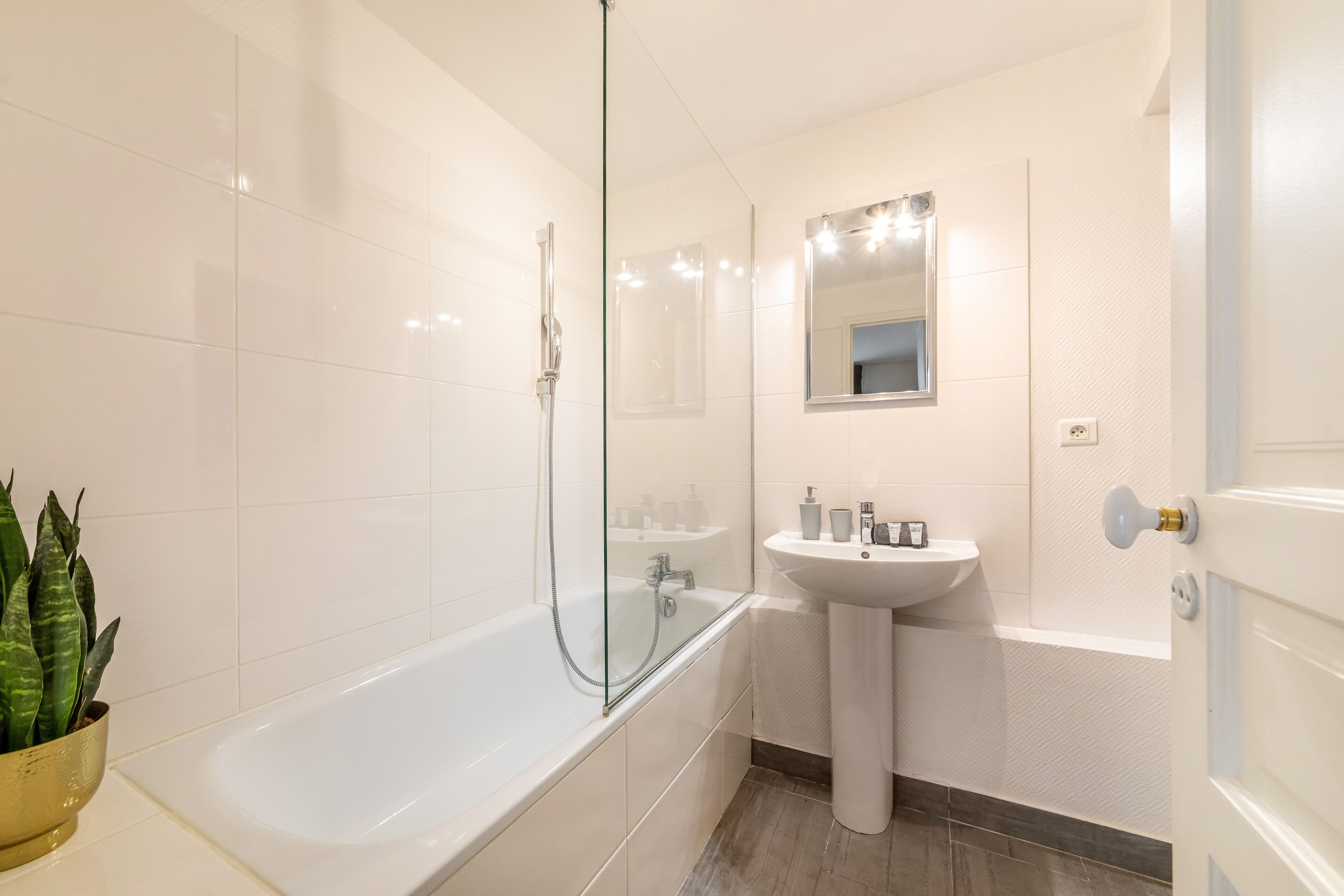 Un baño moderno con ducha de vidrio, lavamanos pedestal y un espejo grande.
