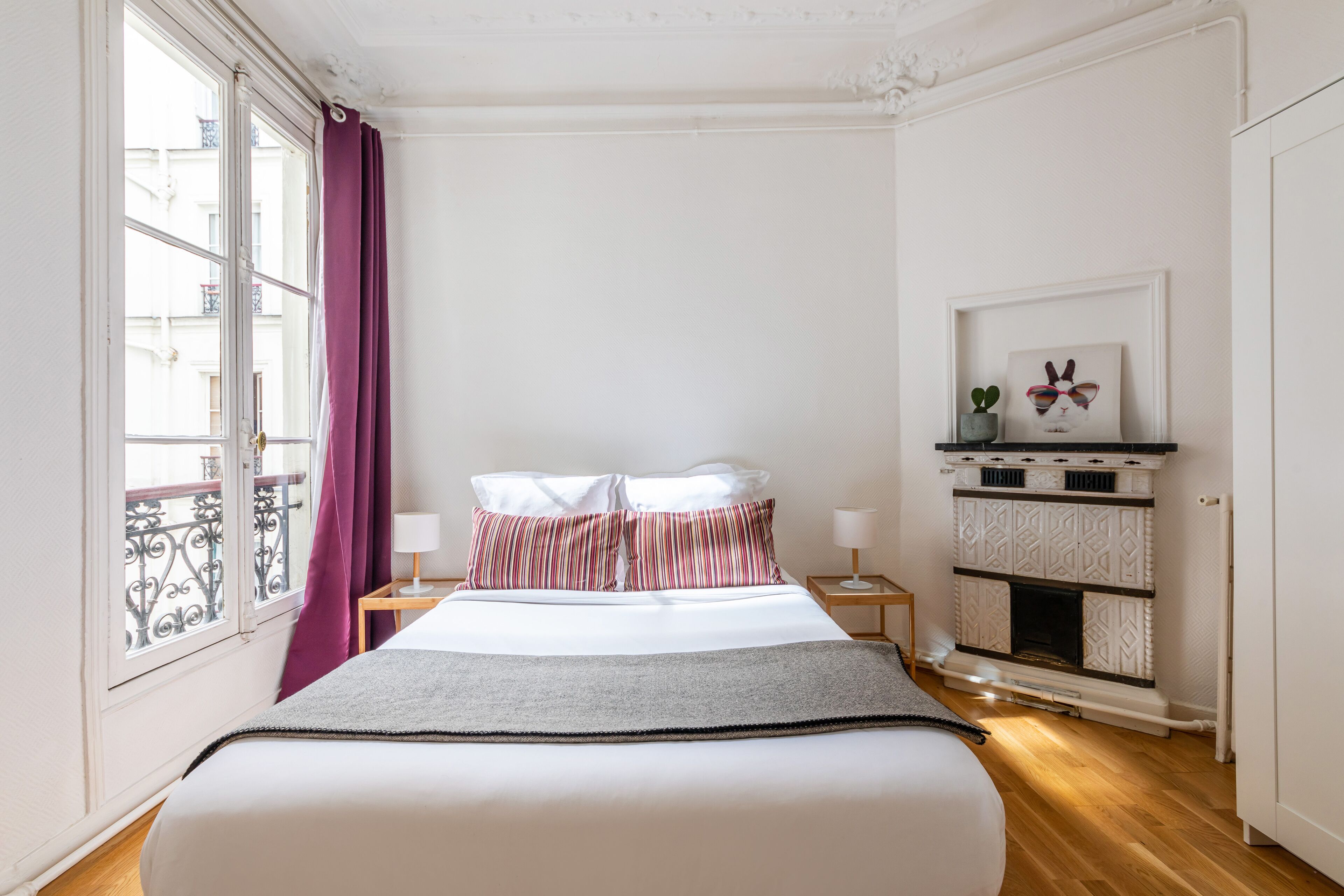 Een slaapkamer met een bed, nachtkastje, open haard en raam met gordijnen.