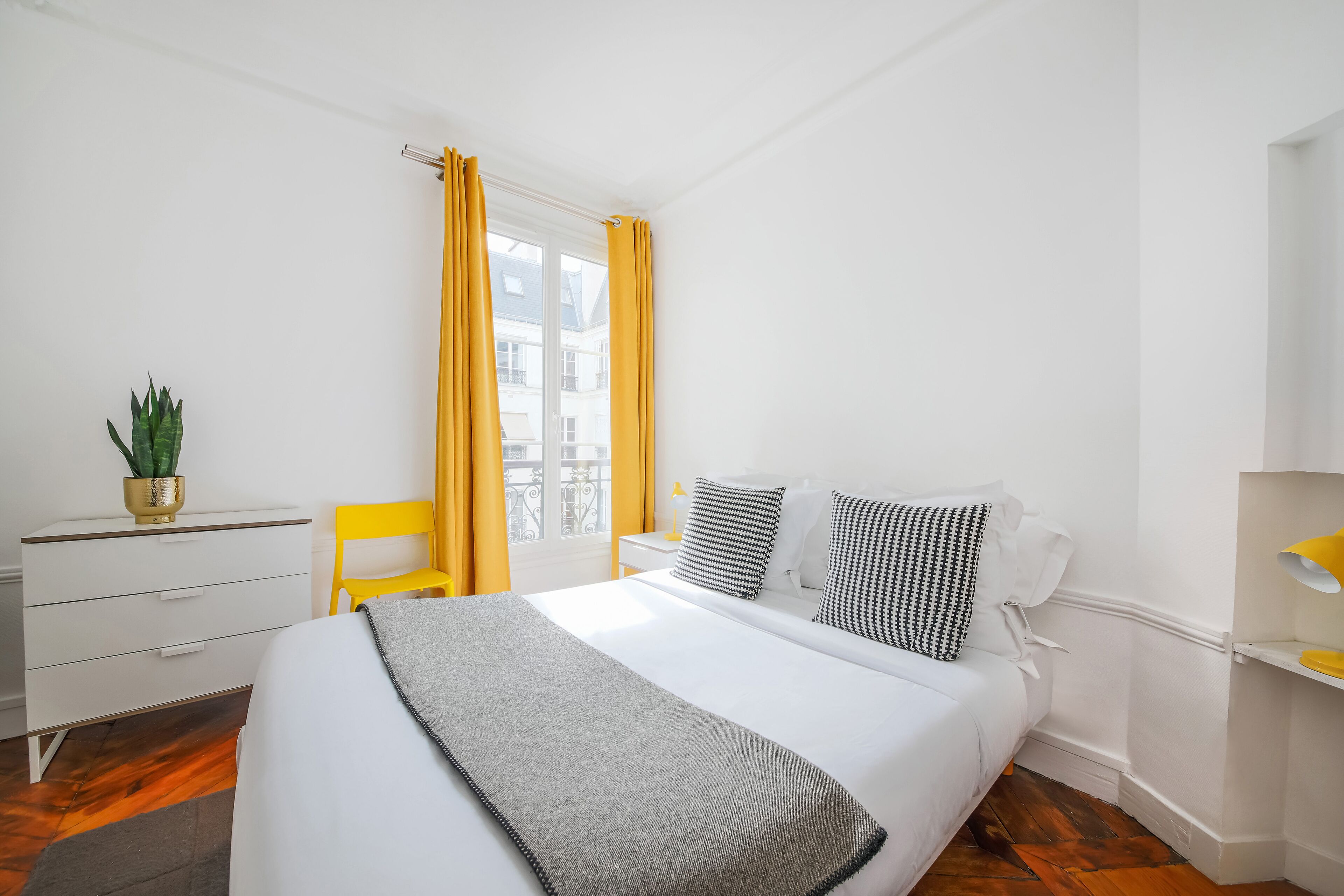 A bedroom with a bed, a desk, a chair, and a window with curtains.