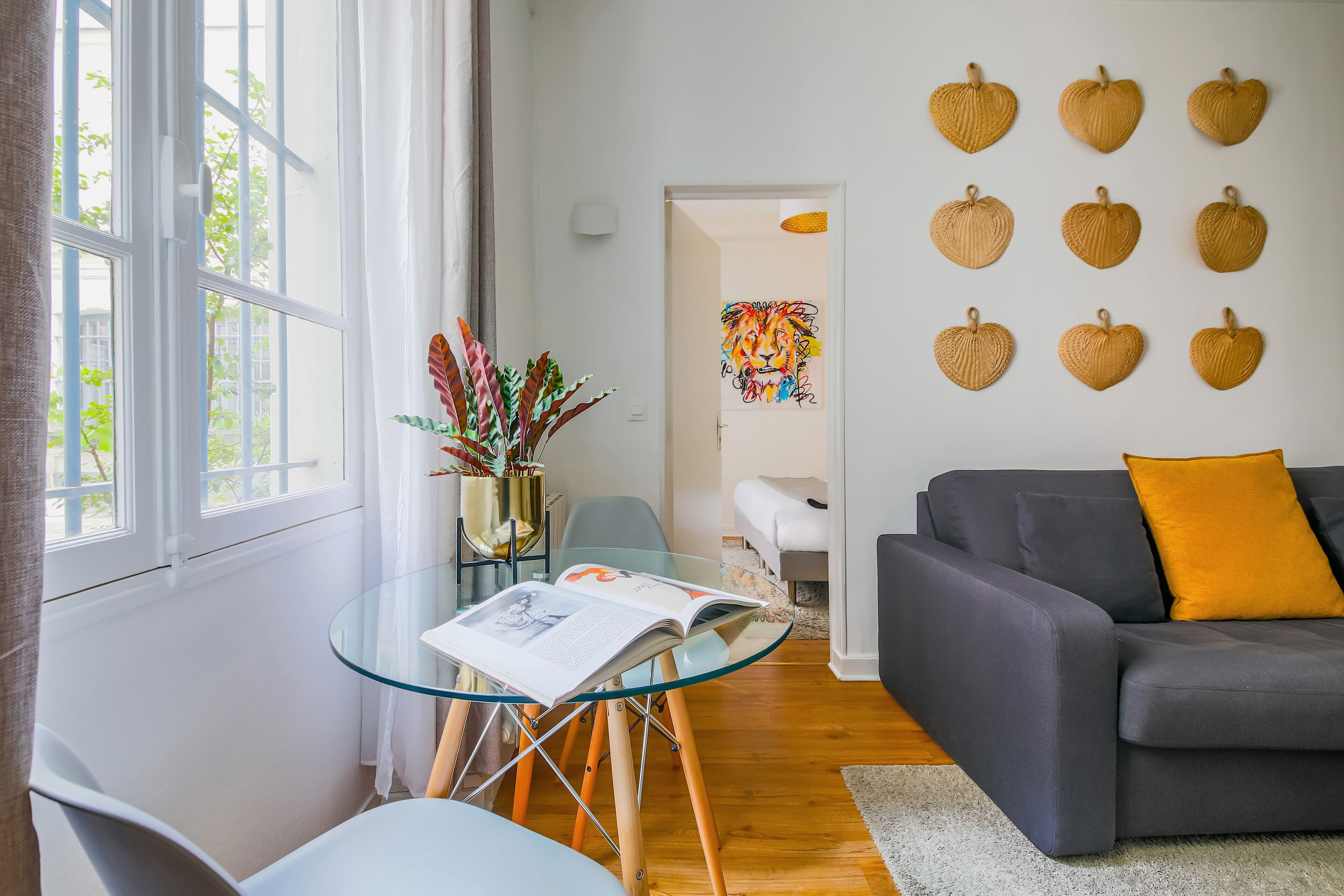 A modern living room with a glass table, a grey sofa, and a wall decorated with heart-shaped ornaments.