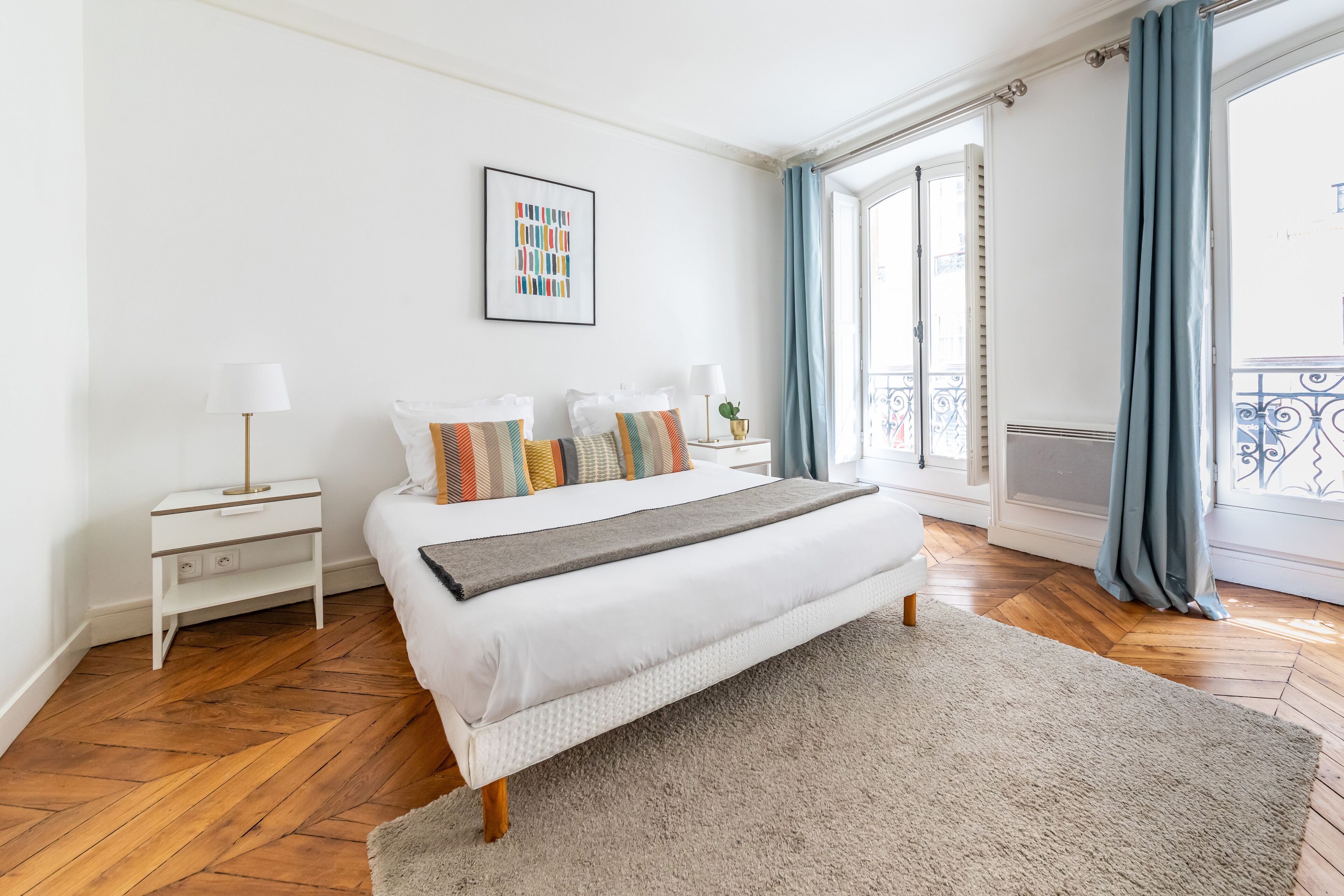 A neatly arranged bedroom with a bed, bedside tables, a rug, and a window with curtains.