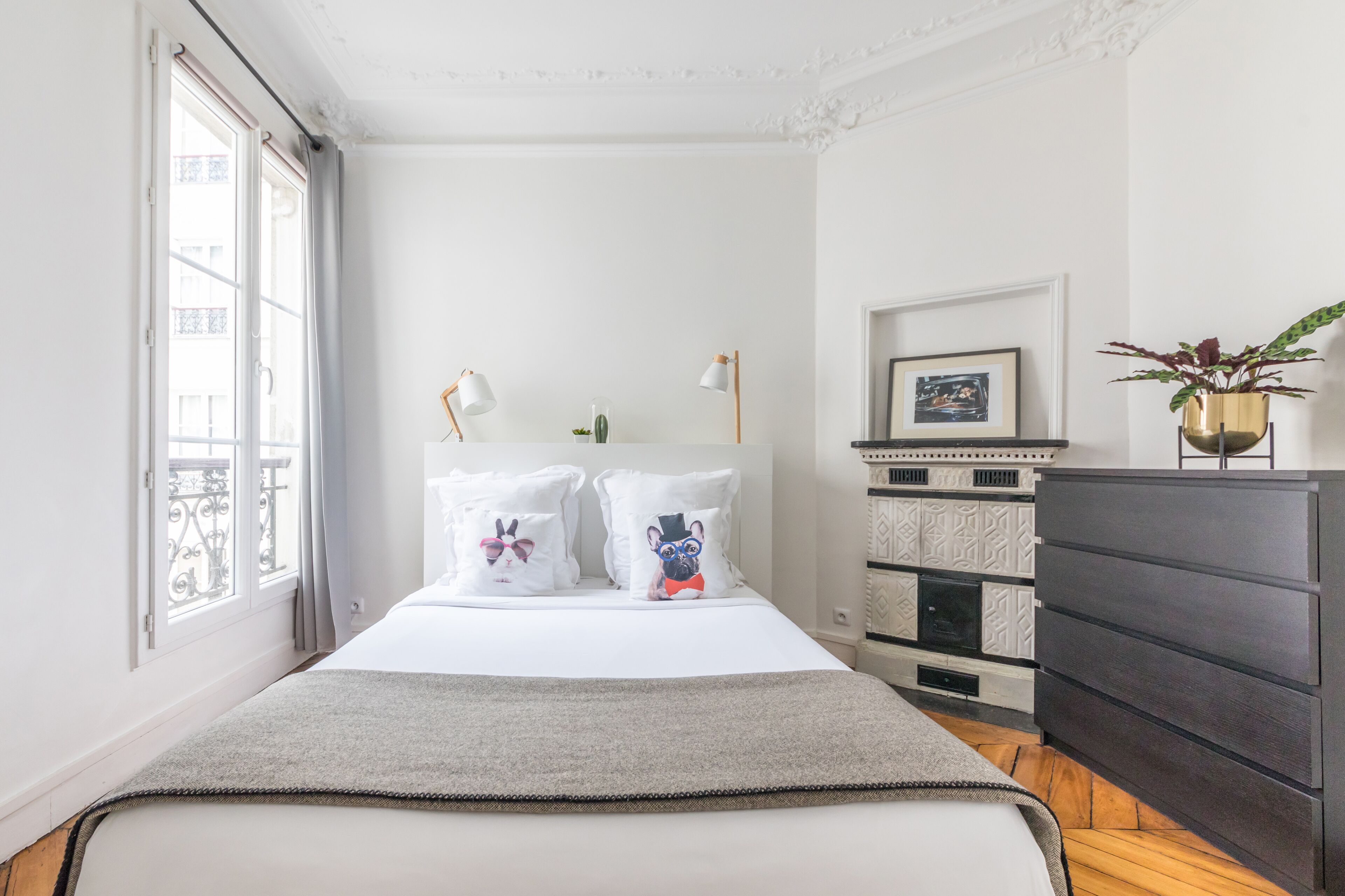 Een slaapkamer met een bed, bedlampjes, een dressoir, een potplant en een lijst met een foto aan de muur.