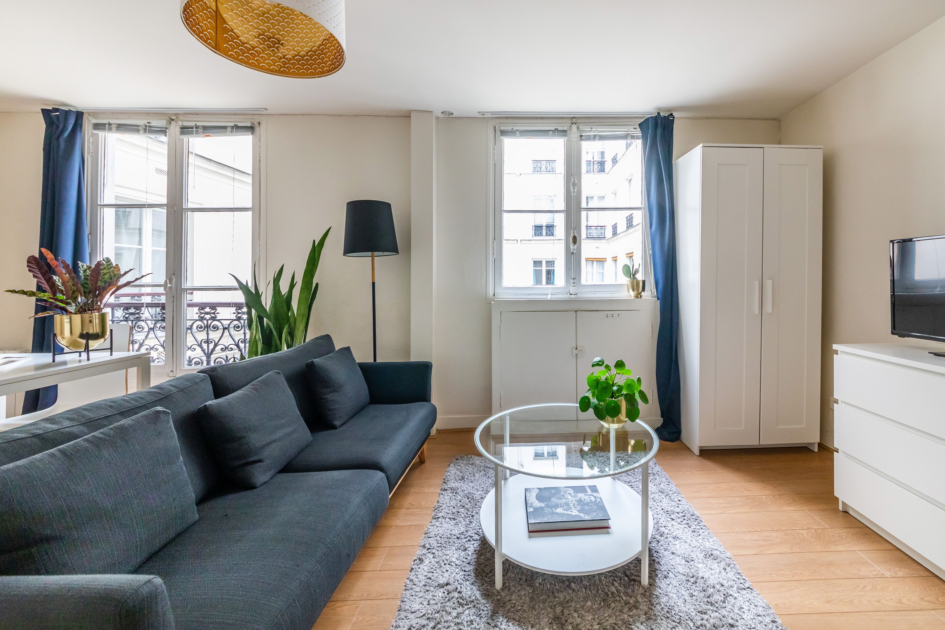 Un salon moderne avec un canapé gris, une table basse en verre et un meuble blanc.