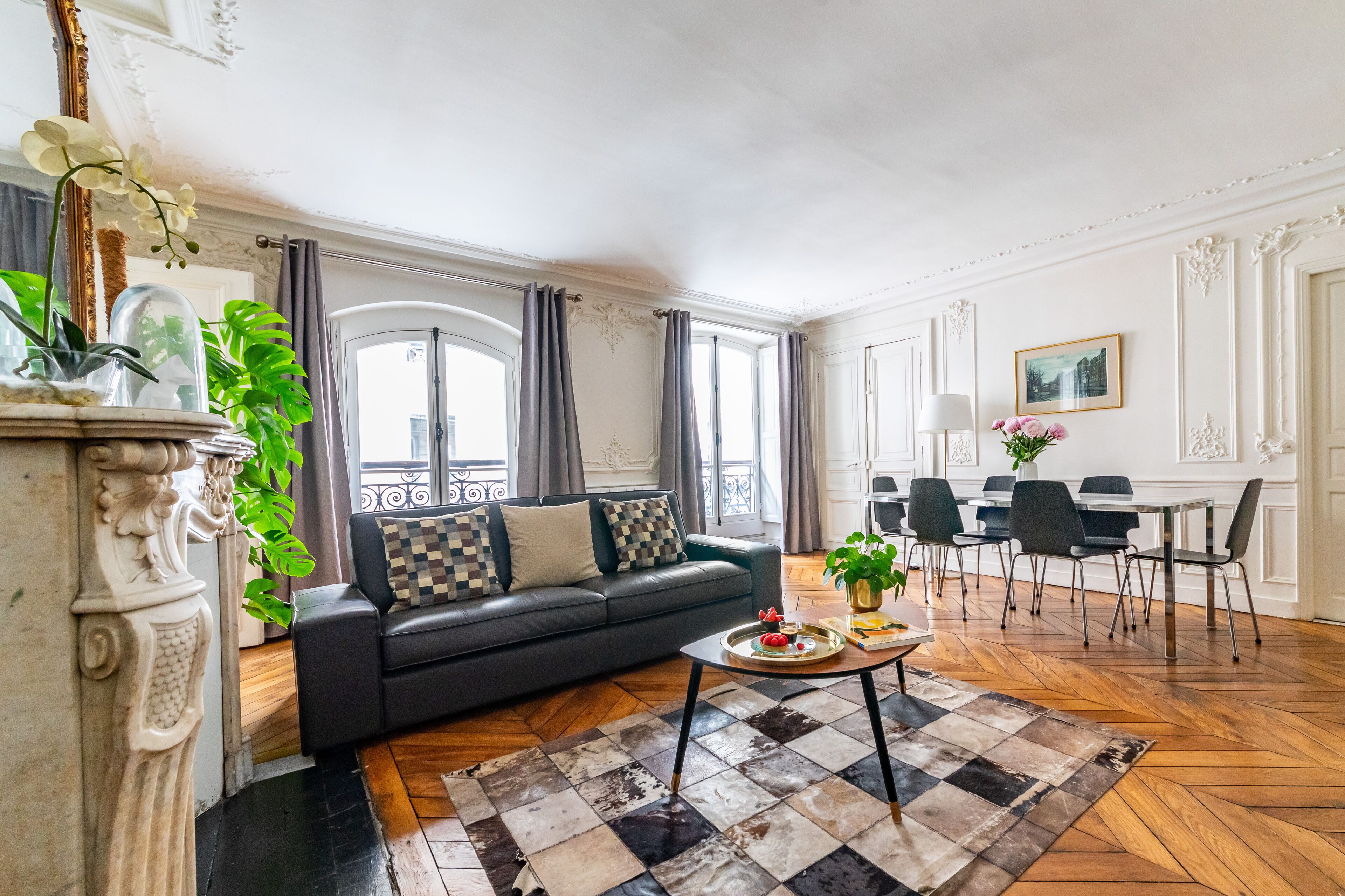 A living room with a black sofa, a coffee table, and a dining area with chairs and a table.