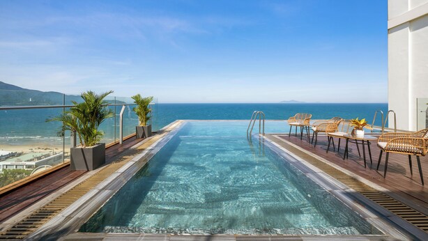 A rooftop infinity pool with a view of the ocean, wooden deck, and outdoor furniture. - Lunar Hotel Danang (Da Nang)
