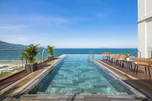 Uma piscina infinita no terraço com vista para o oceano, deck de madeira e mobiliário de exterior.