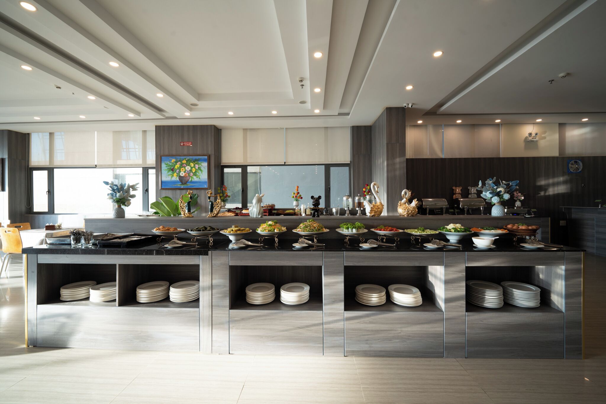 A modern kitchen with a central island, multiple dishware storage shelves, and a variety of food items displayed.