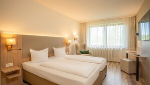 Hotellihuone, jossa on suuri sänky, yöpöytälamput, työpöytä ja tuoli.