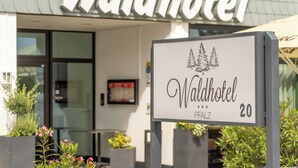 Waldhotel-kyltti, jossa on kuva vuoresta ja mänty puusta, mikä viittaa siihen, että kyseessä on luontoaiheinen majoituspaikka.