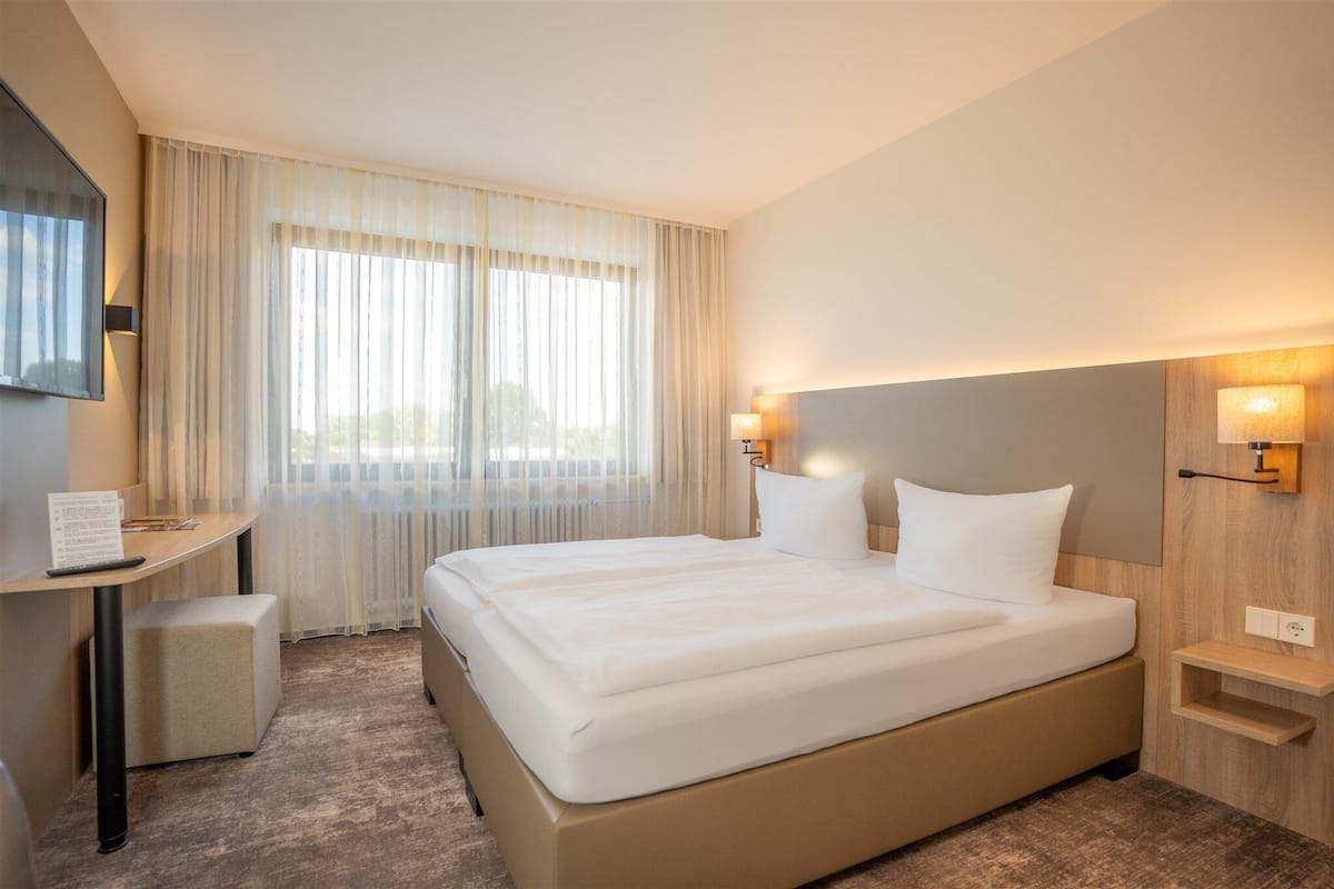 Une chambre d’hôtel avec un grand lit, un bureau avec une chaise, une petite table et un téléviseur fixé au mur.