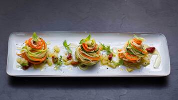 Un plato rectangular con tres preparaciones vegetales en espiral, adornado con hierbas, sobre una superficie oscura.
