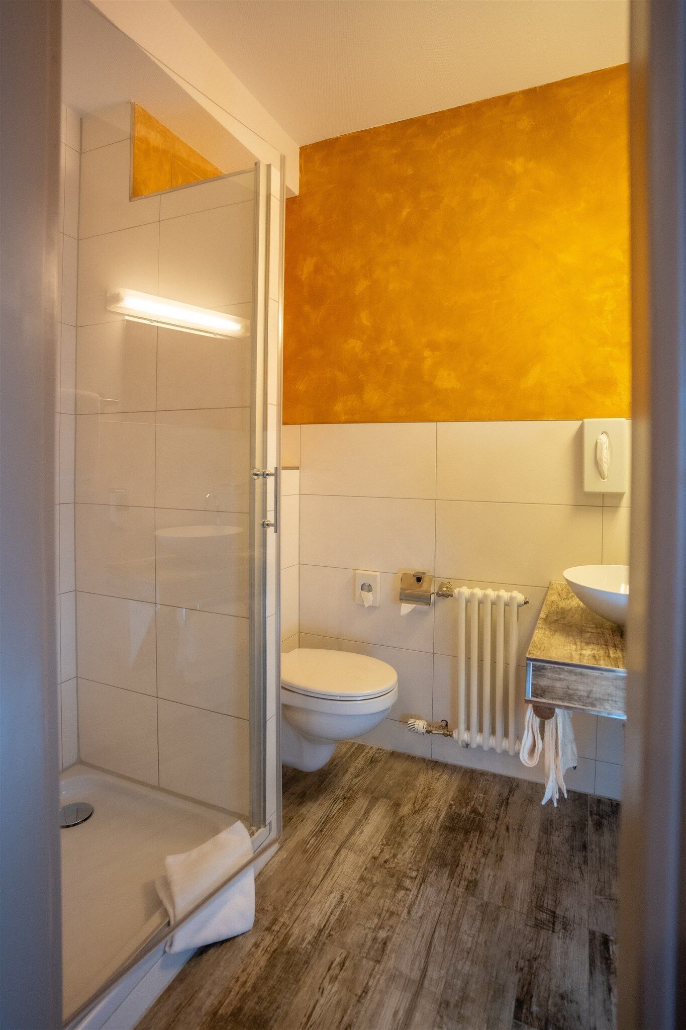 A bathroom with a glass shower enclosure, a white toilet, a wooden vanity, and a yellow accent wall.